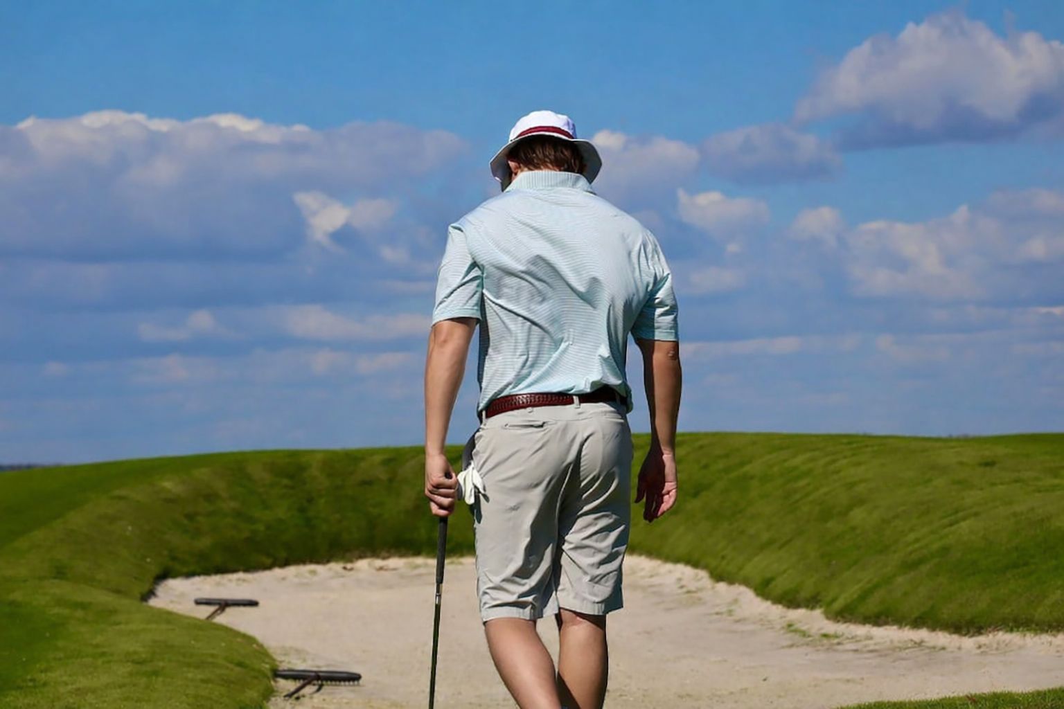 Golfspelare i ljusblå pikétröja och hatt går på en sandbunker på golfbanan.